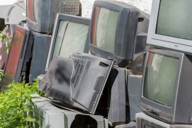 Eski, kirli, kırık elektronik döküntüler otla kaplanmış.
