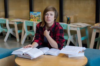 Kütüphanedeki kitapların arasında düşünceli bir öğrenci pencereden dışarı bakıyor.