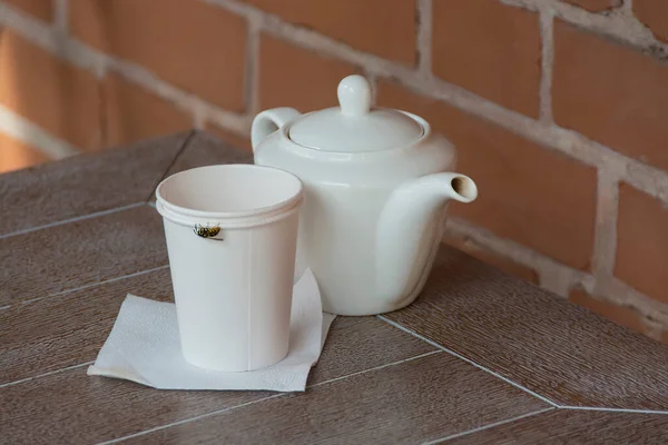 a teapot and disposable cups with a bee on the table of a summer cafe