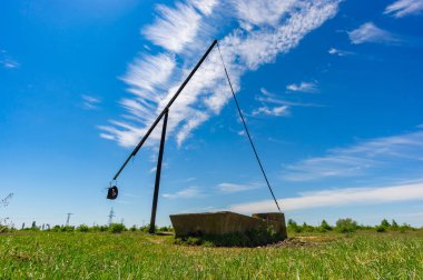 Yazın eski vinç sahada. Yakınlarda inekler için beton içici var. Sirus bulutları ve uzak ufuklarıyla mavi gökyüzü