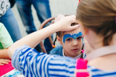 Peri masalı karakterine bürünmüş bir kadının yüzü. Yüze mavi bir su rengi uygulanıyor.