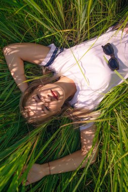 Tişört tasarım konsepti. Güzel bir kız çimenlerde beyaz tişörtle yatıyor.