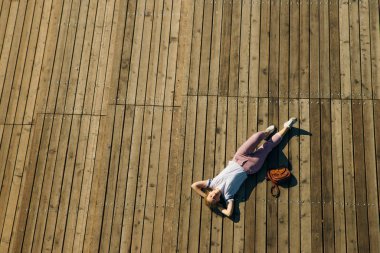 Hippi genç kadın ahşap zeminde yatıyor. Kot pantolon ve güneş gözlüklü beyaz bir tişört giy..