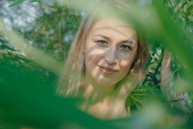 Sarışın kız, gün batımında yeşil çalılıklarda.