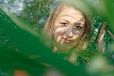 Sarışın kız, gün batımında yeşil çalılıklarda.