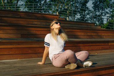 Ahşap zeminde oturan genç hippi kadın. Kot pantolon ve beyaz tişört giyiyor.