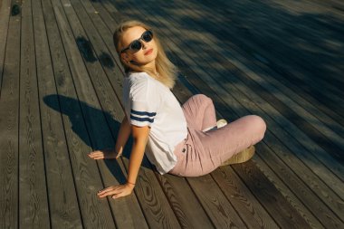 Ahşap zeminde oturan genç hippi kadın. Kot pantolon ve beyaz tişört giyiyor.