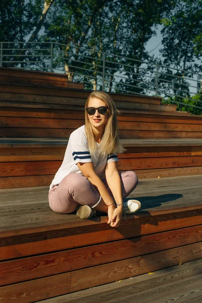 Młoda hipsterka siedząca na drewnianej podłodze. W dżinsach i białej koszulce. — Zdjęcie stockowe