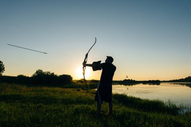 A silhouette of an archer drawing his bow and aiming upwards clipart