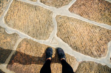 Taş kaldırımda duran ayakkabılar içinde iki ayak. Doğrudan görünümün üstünde.