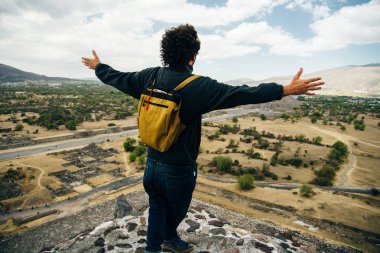 Teotihuacan, Meksika. Sırt çantası ve şapkalı Meksikalı Amerikalı bir turist, Piramidin tepesinden manzaranın keyfini çıkarır. Güneş