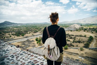 Teotihuacan, Meksika. Sırt çantası ve şapkalı Meksikalı Amerikalı bir turist, Piramidin tepesinden manzaranın keyfini çıkarır. Güneş