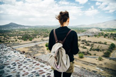 Teotihuacan, Meksika. Sırt çantası ve şapkalı Meksikalı Amerikalı bir turist, Piramidin tepesinden manzaranın keyfini çıkarır. Güneş
