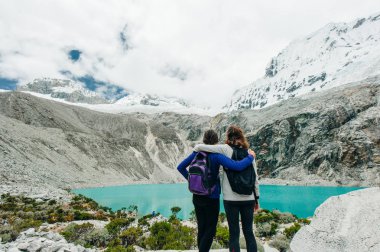 Laguna 69, Peru. Sırtı mavi göle dönük, kot pantolonlu, sarı ceketli bir kız.