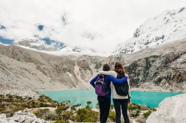 Laguna 69, Peru. Sırtı mavi göle dönük, kot pantolonlu, sarı ceketli bir kız.