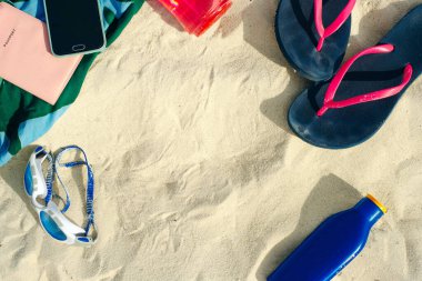 tatil ve yaz tatili konsepti - parmak arası terlikler, havlu, kapak, şişe su ve kumsalda bir şişe güneş yağı.