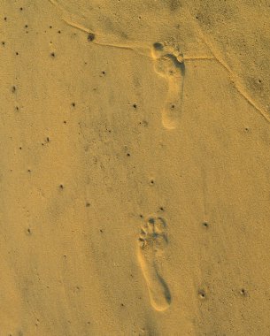 Kumda bir çift ayak izi. Ayak izleri geride bıraktıklarımızı sembolize eder; onlar bir iz, bir girinti. Birinin daha önce buraya geldiğini ve şu anda geçmekte olduğu yoldan geçtiğini gösteriyor..