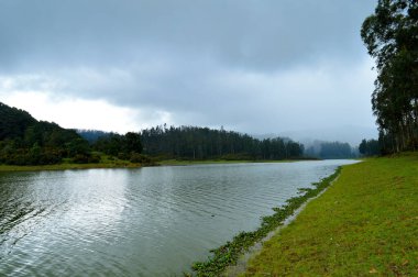 Arka planda sisli tepeler ve ağaçlar olan güzel bir su deposu. Kara, yağmur mevsiminde yeşildir. Bazı elektrik hatları ve kuleler dışında doğanın gerçek güzelliği görülebilir..