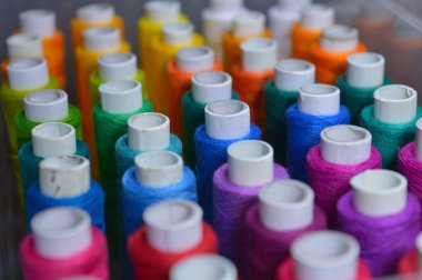 Renkli iplik ruloları bir kutuda düzenlenmiş. Resmin bazı kısımları infocus. Tekstil endüstrisini ve terzileri temsil eder..