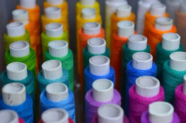 Renkli iplik ruloları bir kutuda düzenlenmiş. Resmin bazı kısımları infocus. Tekstil endüstrisini ve terzileri temsil eder..