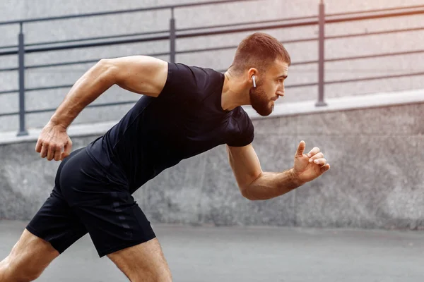 Sporcu adam koşmaya başladı. Genç adam koşuyor. Endüstriyel kentte hızlı koşan bir koşucu. Spor, atletizm, fitness, koşu aktivitesi. Egzersiz, yaşam tarzı konsepti. Başlangıç için koşucu..
