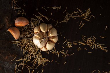 Siyah arka planda ahşap tabakta sarımsak ve biberiye. Tahta masadaki biftekler için taze ve kurutulmuş taze otlar..