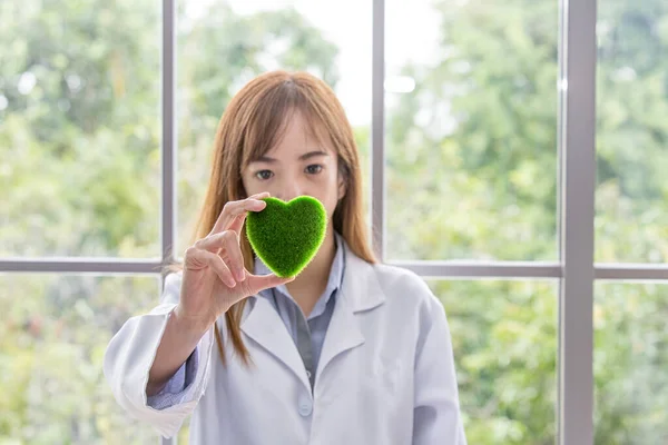 Science whit green spirit mind. Green heart in her hand on lab a background. Beautiful smiling female doctor or Scientist holding organic heart-shaped. asian lab. science room