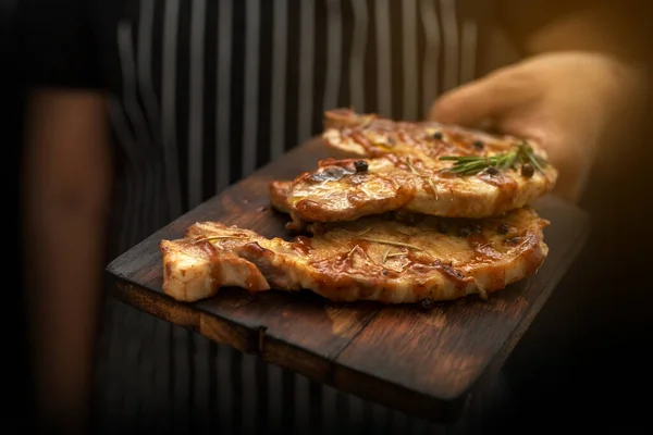 Image cooking on kitchen. Master Chef holding steak. Woman Chef kitchen holding grilled beef steak on plate with organic vegetable decoration. beef or pock. T-bone on wooden. Morning Light.