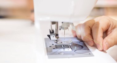Yakın çekim. Dikiş makinesiyle çalışan kadın terzi. Dikiş makinesindeki iplikle dikiş işi yaparken profesyonel kadın elleri..