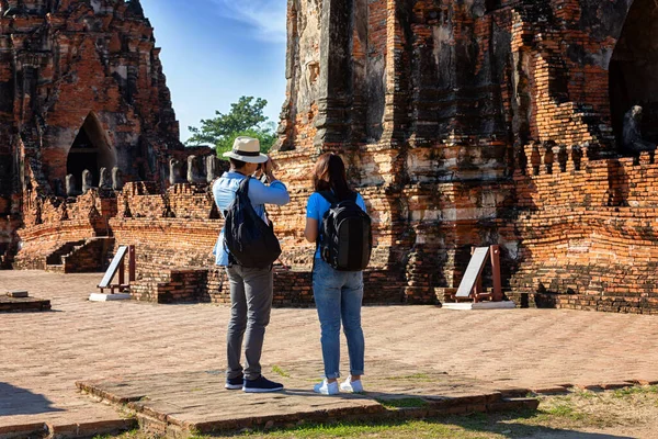 Doğu Asya yaz tatili. Beyaz adam ve Asyalı kadın turist Wat Chaiwatthanaram tapınağına bakıyorlar. Turistler sabahları Tayland 'ın Ayutthaya kentindeki tapınakta seyahat ediyorlar..
