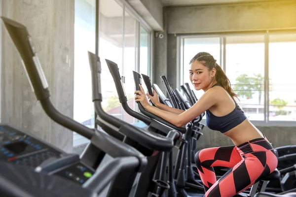 The female is cycling in the gym. Portrait of girl exercising on cardio machines in the sport club. Pretty women body builder working out at the gym. asian people.