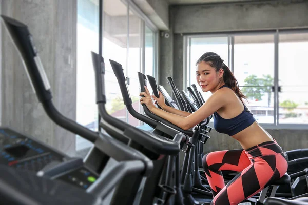 The female is cycling in the gym. Portrait of girl exercising on cardio machines in the sport club. Pretty women body builder working out at the gym. asian people.