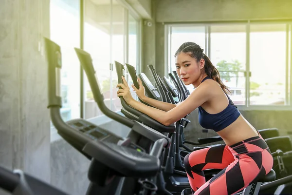 The female is cycling in the gym. Portrait of women exercising on cardio machines in the sport club. Pretty girl body builder working out at the gym.