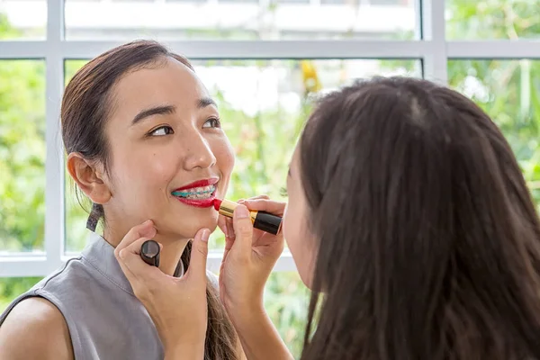 Beauty woman take lipstick, Girl friends helping with make-up. Girlfriends fooling around with makeup. Two smiling woman applying make up at home. Asian female.