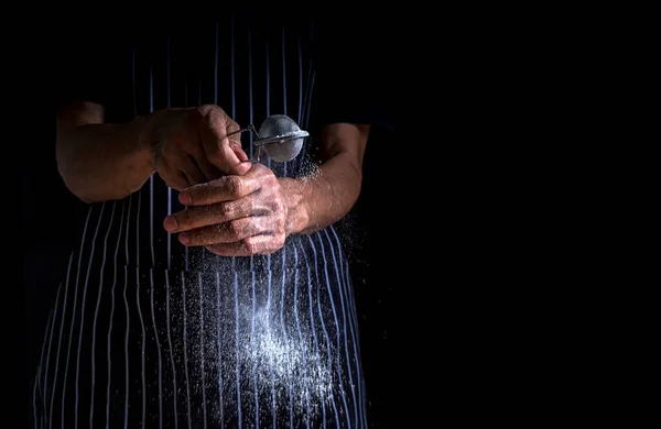 Chef sprinkle icing sugar on the donut. Male baker sprinkles sweet donuts with powder and icing sugar on black background.