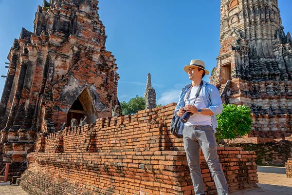 Travelers traveling to Asia. Eastern Asia summer holidays. Caucasian man tourist looking at Wat Chaiwatthanaram temple. Tourist travel in the morning at temple in old city of Ayutthaya in Thailand.