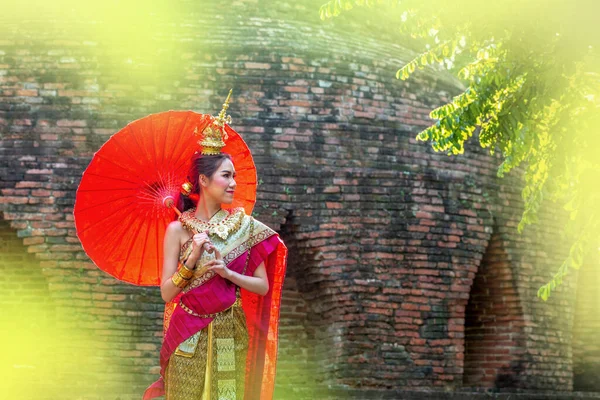 Thai Woman In Traditional Costume with umbrella of Thailand. Female  Traditional Costume with thai style temple background. Wat Chaiwatthanaram temple in Ayuthaya is Unesco World Heritage.