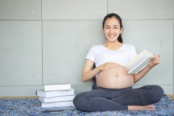 Pregnant mothers are reading books. Happy pregnant asian woman reading book on carpet at home.