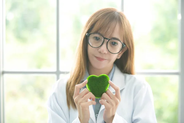 Science whit green spirit mind. Green heart in her hand on lab a background. Beautiful smiling female doctor or Scientist holding organic heart-shaped. asian lab. science room