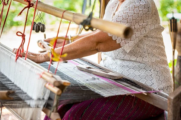 Traditional Isan Thai silk weaving. old woman hand weaving silk in traditional way at manual loom. Thailand. Selective focus.