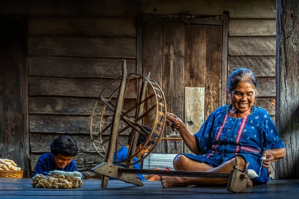 Older women in the community are pushing cotton into a thread for weaving for indigo dyeing