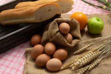 Kahvaltı ve fırında ekmek konsepti. Kumaş çuvalında taze kokulu ekmek, yumurta ve elma. Tahta masada..