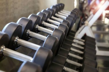 Spor için motivasyon. Dumbbell salonda oynuyor. Spor salonunun arka planında spor aletleri. Yan görüş. Seçici odak.