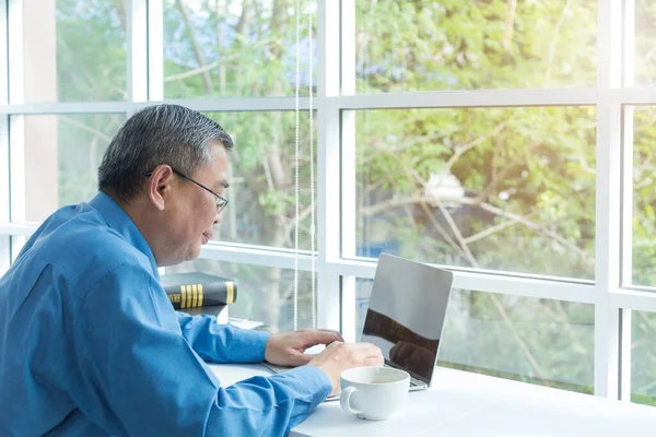 A man working in a coffee shop. Men at cafe using laptop. Asian man sitting in a coffee shop busy working on he laptop.