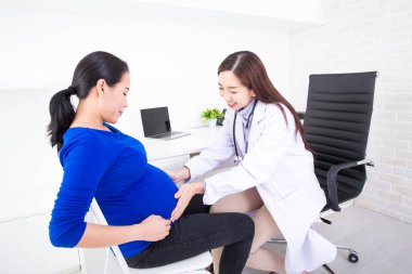 Doktor hamileliği inceliyor. Genç doktor klinikte hamile kadını muayene ediyor. Steteskoplu hamile kadın doktor..