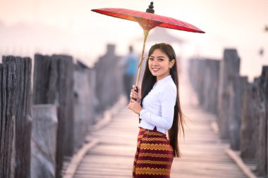 Genç bir Burmalı kadın Asya 'nın en uzun meşe köprüsünde kırmızı şemsiyeyle yürüyor. U-bein köprüsü, Mandalay, Myanmar.