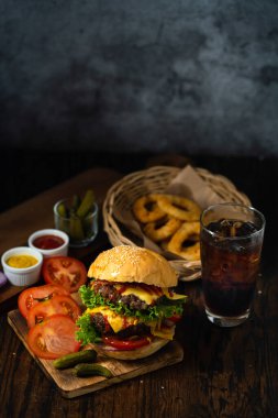 Taze ve sulu hamburger. Hamburgerler ve meşrubatlar ahşap zemine konur. Biftek ya da pastırmalı çizburger, domates, soğan halkası ve köpüklü su..