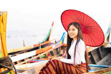 Asyalı bir kadın elinde kırmızı bir şemsiyeyle gondolda oturuyor. Mandalay, Myanmar 'da, Asya' daki köprüde, tahta teknede kırmızı şemsiyeli genç bir Burmalı kadın..
