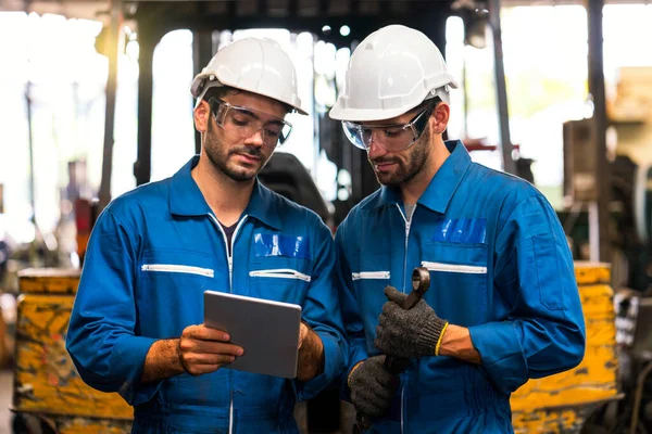 Endüstriyel bir forkliftin önünde duran bir İngiliz anahtarı ve tablet tutan tamirci.