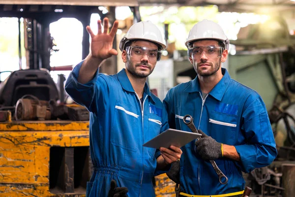 Endüstriyel bir forkliftin önünde duran bir İngiliz anahtarı ve tablet tutan tamirci. Mühendisler ve yetenekli teknisyenler dört gözle bekliyor..